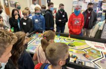 Students gather around the competition board