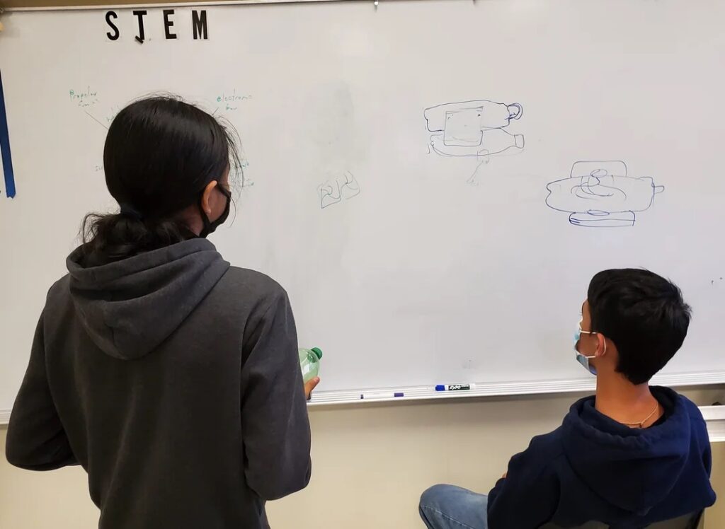 Students sketch out a design on the classroom whiteboard. 