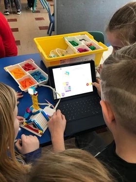 Three students gather around a laptop, programming a Lego. 