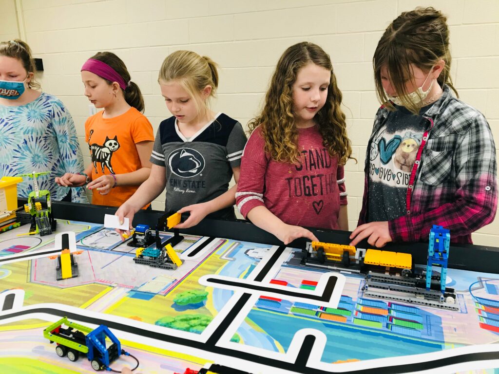 Five students gather behind a competition table, working on various robot pieces. 