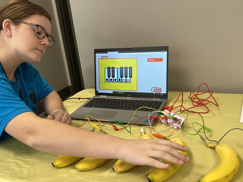 A woman works with a banana piano: bananas connected to a laptop with Makey Makeys. 