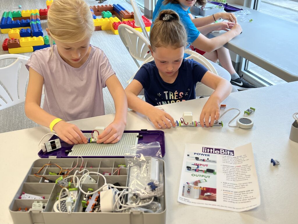 Two children sit at a table and work with Little Bits. 