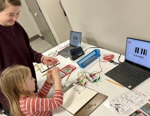 A child works on connecting Makey Makeys to a pencil drawing with the help of an adult.