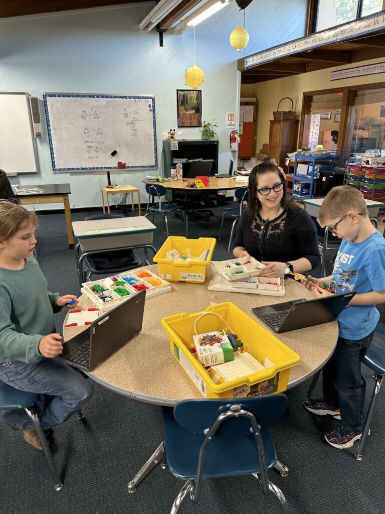 Educator Amanda sits with two of her students at a classroom table, working with Lego Spikes.