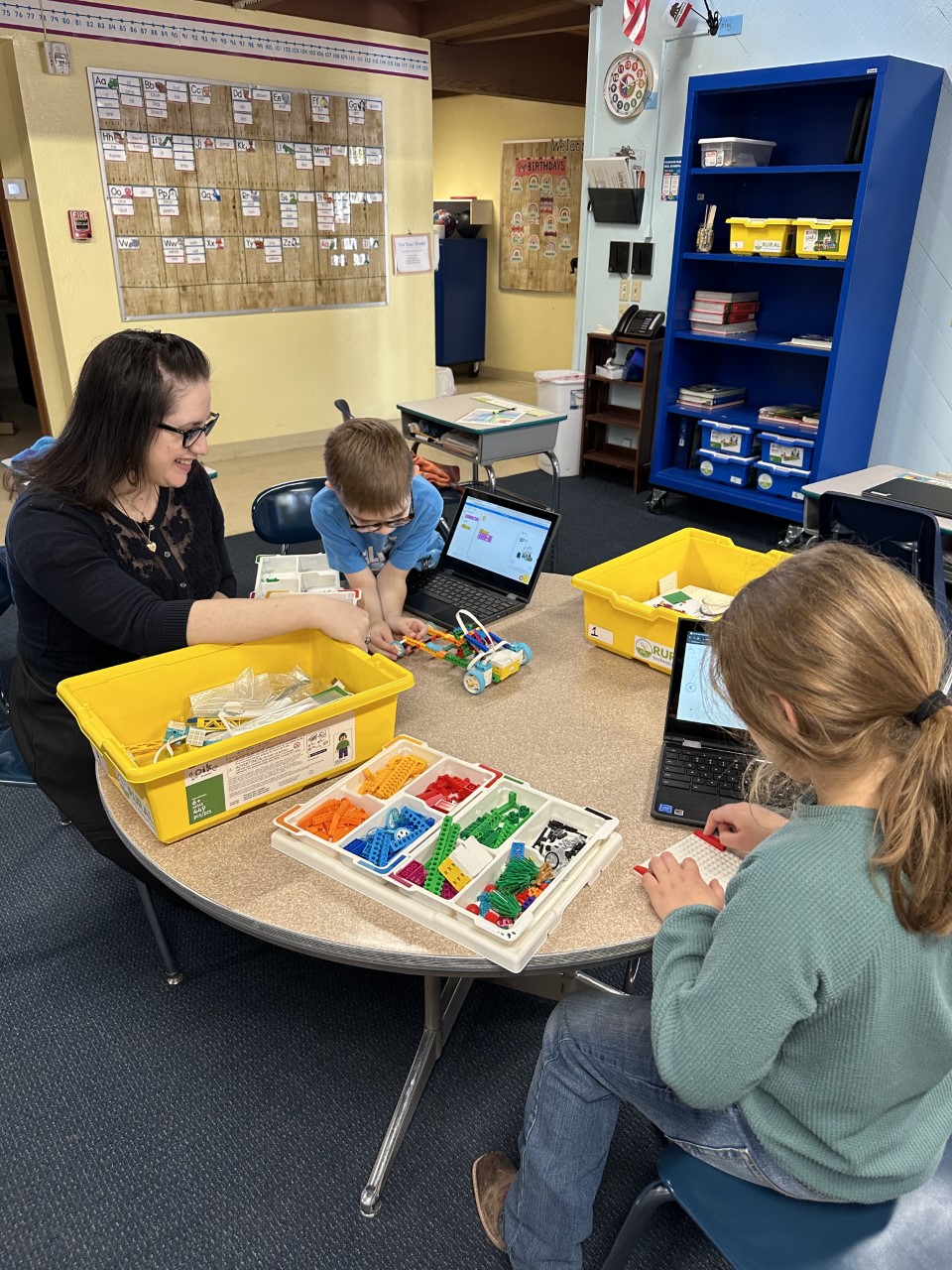 Educator Amanda sits with two of her students at a classroom table, working with Lego Spikes.