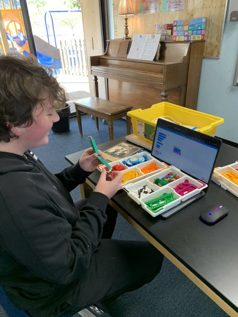 A student sits smiling at a table, working with a LEGO Spike. 