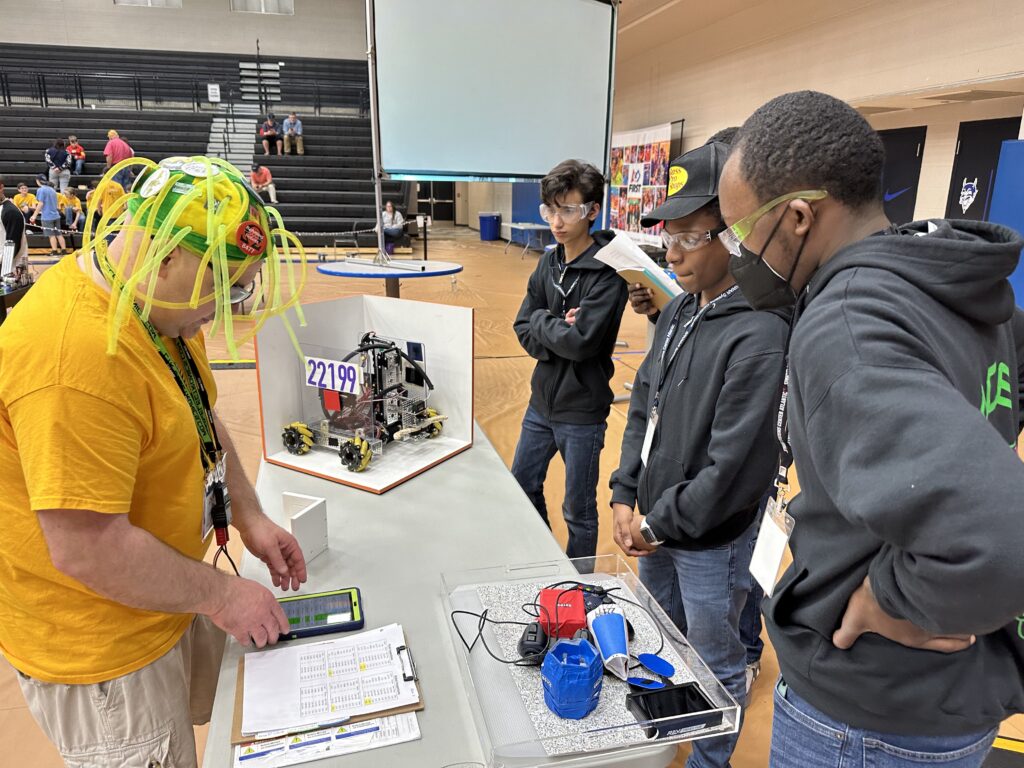 Team members stand at a table with their robot, looking at a judge. 