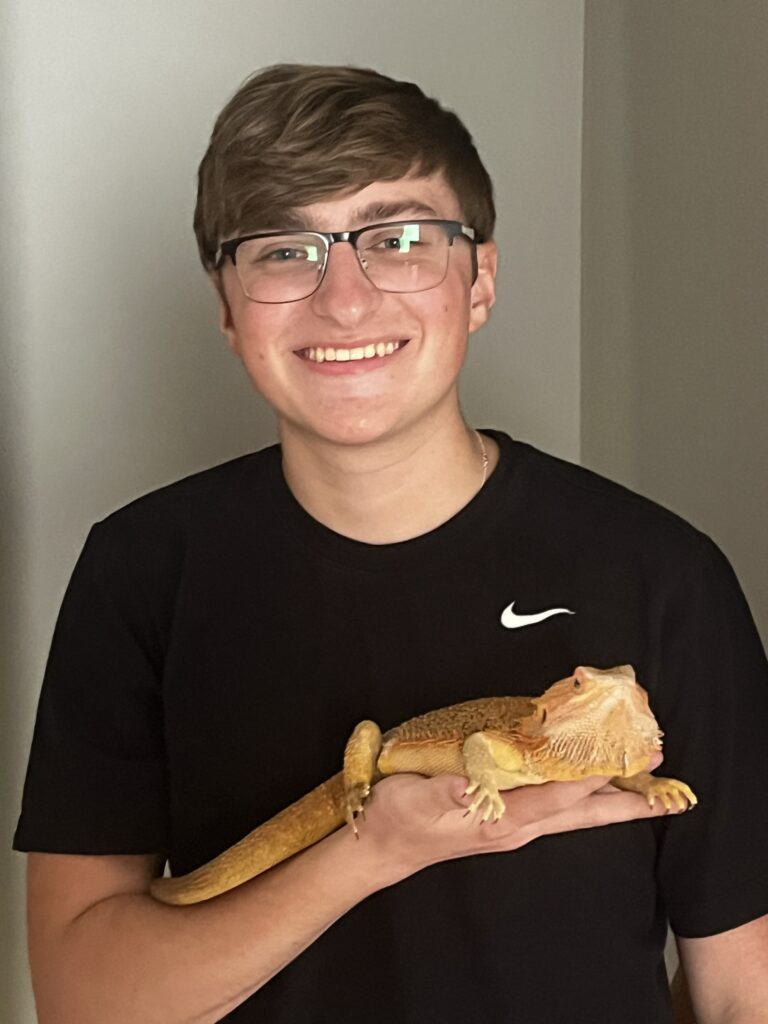 A photo of Connor, smiling and holding a large lizard in his hand. 