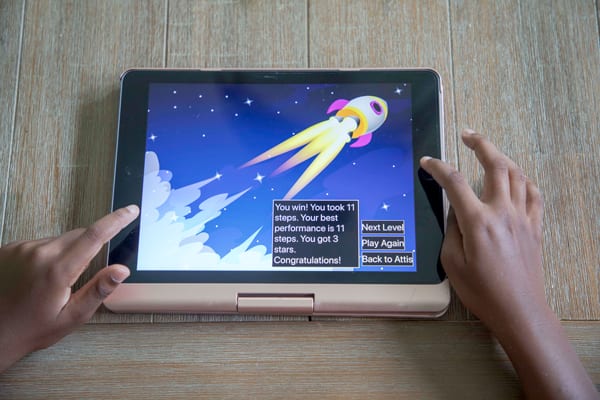 An iPad screen displays an image from the CodeQuest app, showing a rocket blasting into space. 