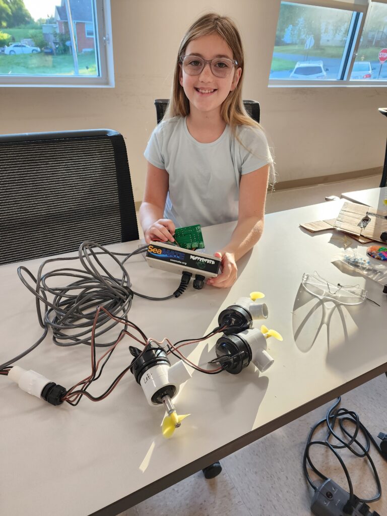 A camper sits at a table with various pieces of equipment for the underwater robot. 