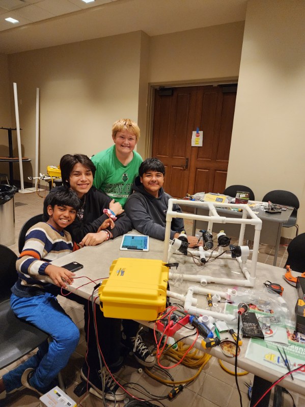Four campers sit at a table that is covered in robotics equipment for their underwater robot.