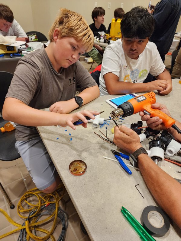 Two campers sit at a table, learning about how to construct part of their robot. 