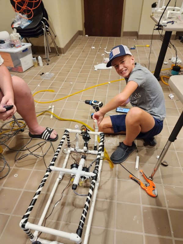 A camper sits on the floor, constructing a robot frame. 