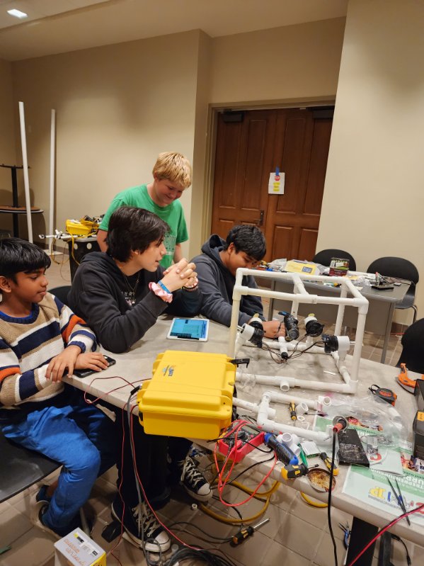 Students gather around a table covered in robotics equipment, constructing their robot. 