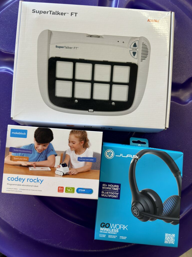 A few items in the library, including a SuperTalker AAC device, a Codey Rocky STEM toy, and a microphone headset for speech-to-text and text-to-speech features. 