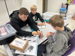 Three students sit at a table, working on constructing a TEXTRIX Robot.