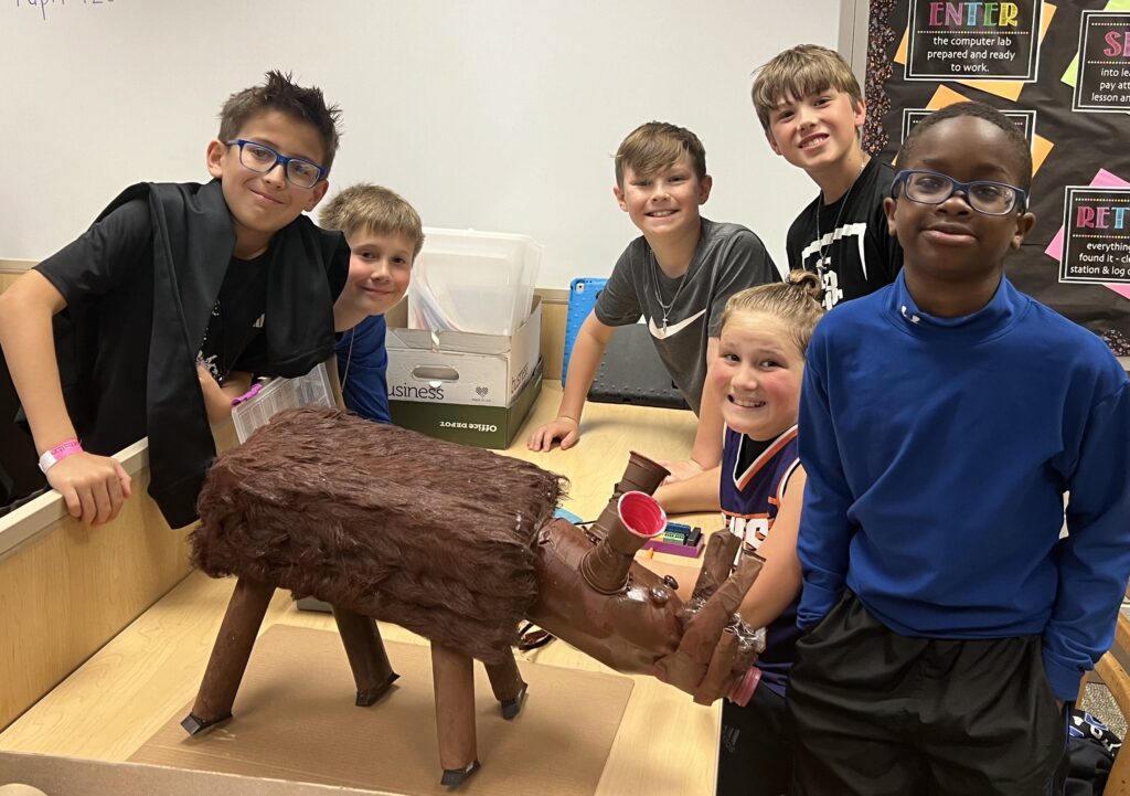 Six students stand around their recyclable and robotics animal creation. 