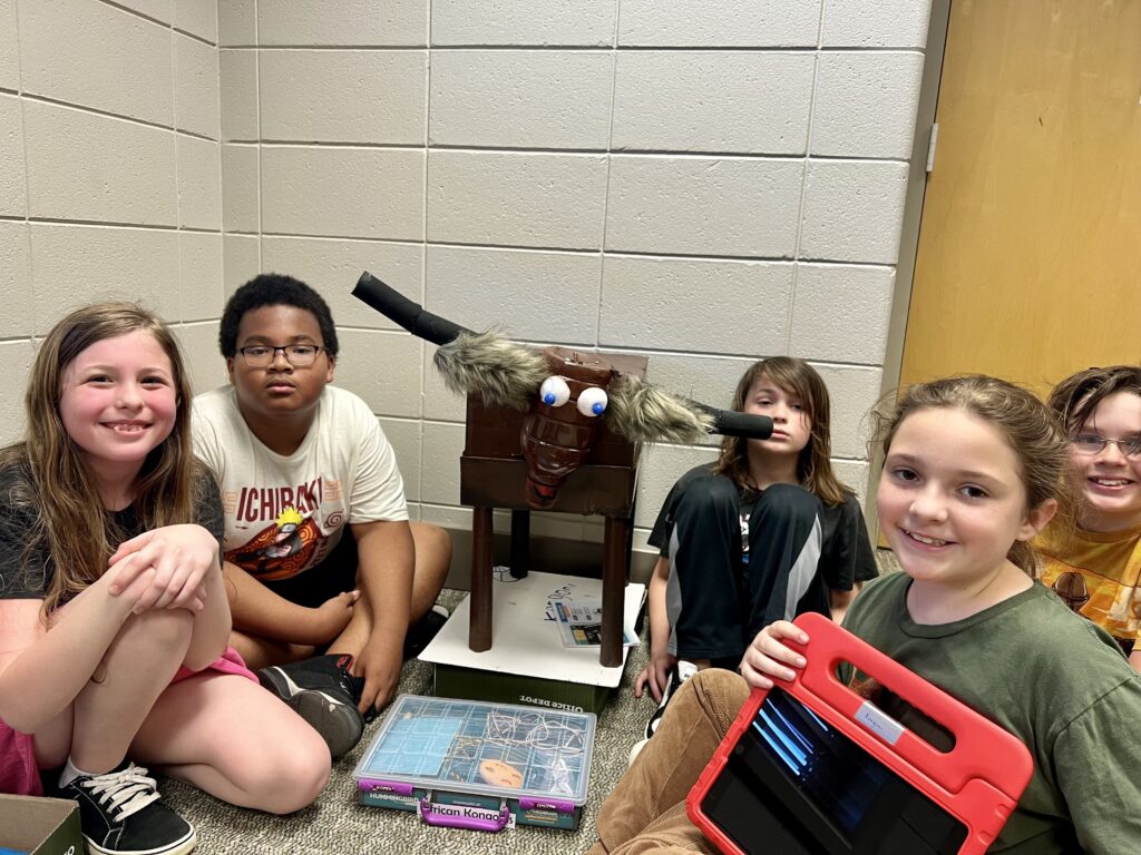 Five students sit with their robotic animal, a Hummingbird robotics kit, and an iPad. 