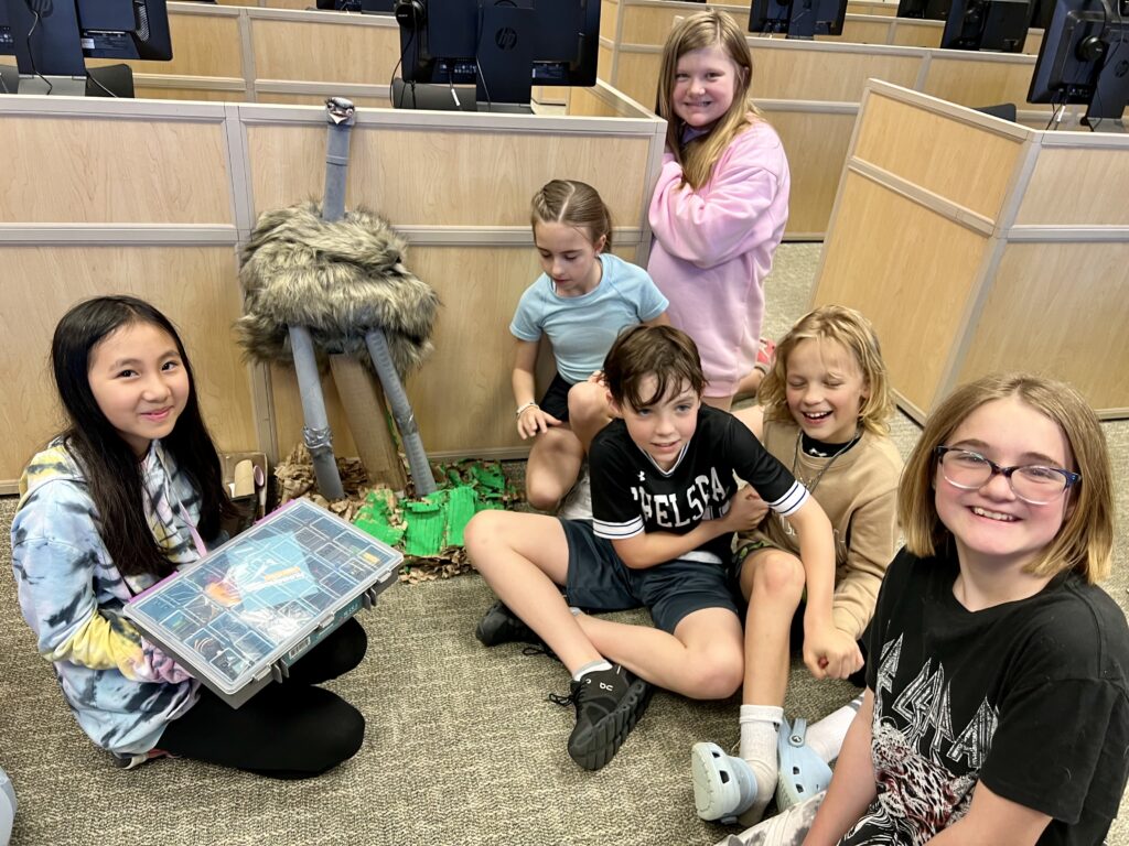 Students with on the floor of a classroom, gathered around their robotic animal creation. 