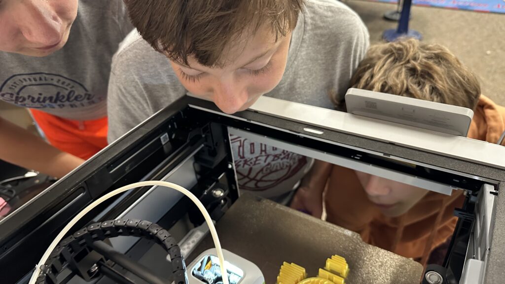 Students peek into a 3D printer, watching their creation come to life. 