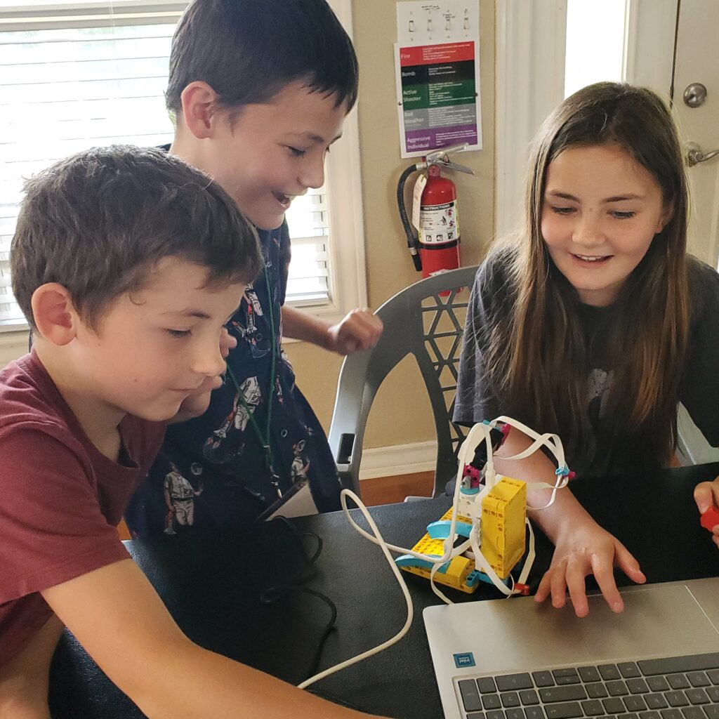 Three students work on assembling and coding a LEGO Spike on a Chromebook.