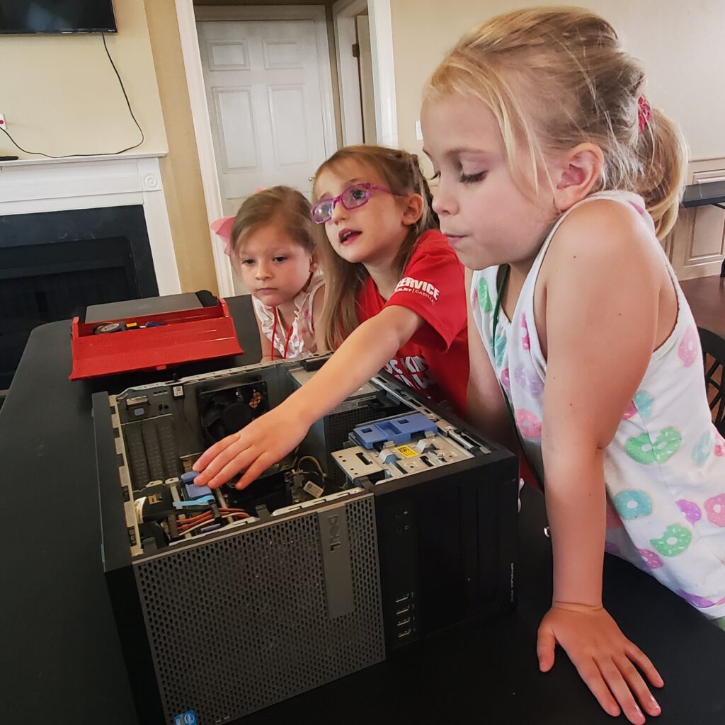 Three students work on a partially deconstructed computer. 