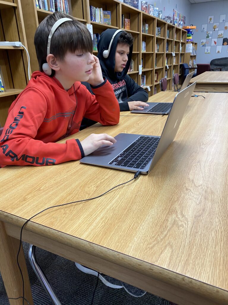 Two students work on laptops with headphones.