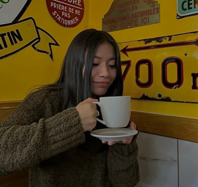 A photo of student Ashley Antunez, holding a coffee mug and smiling at it.