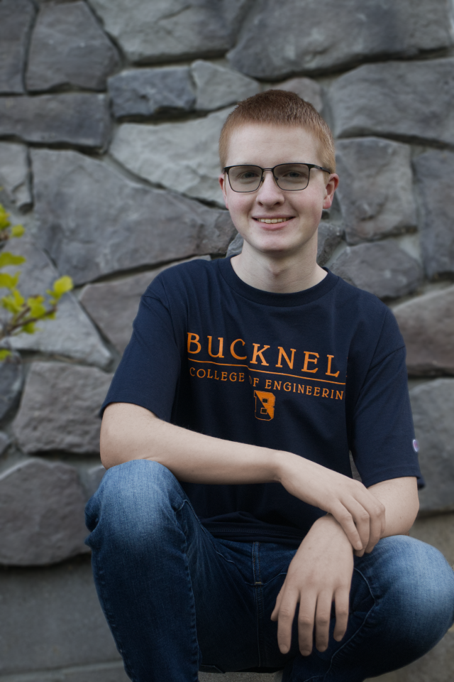A photo of student Caden Purcell, kneeling and smiling in a Bucknell t-shirt.