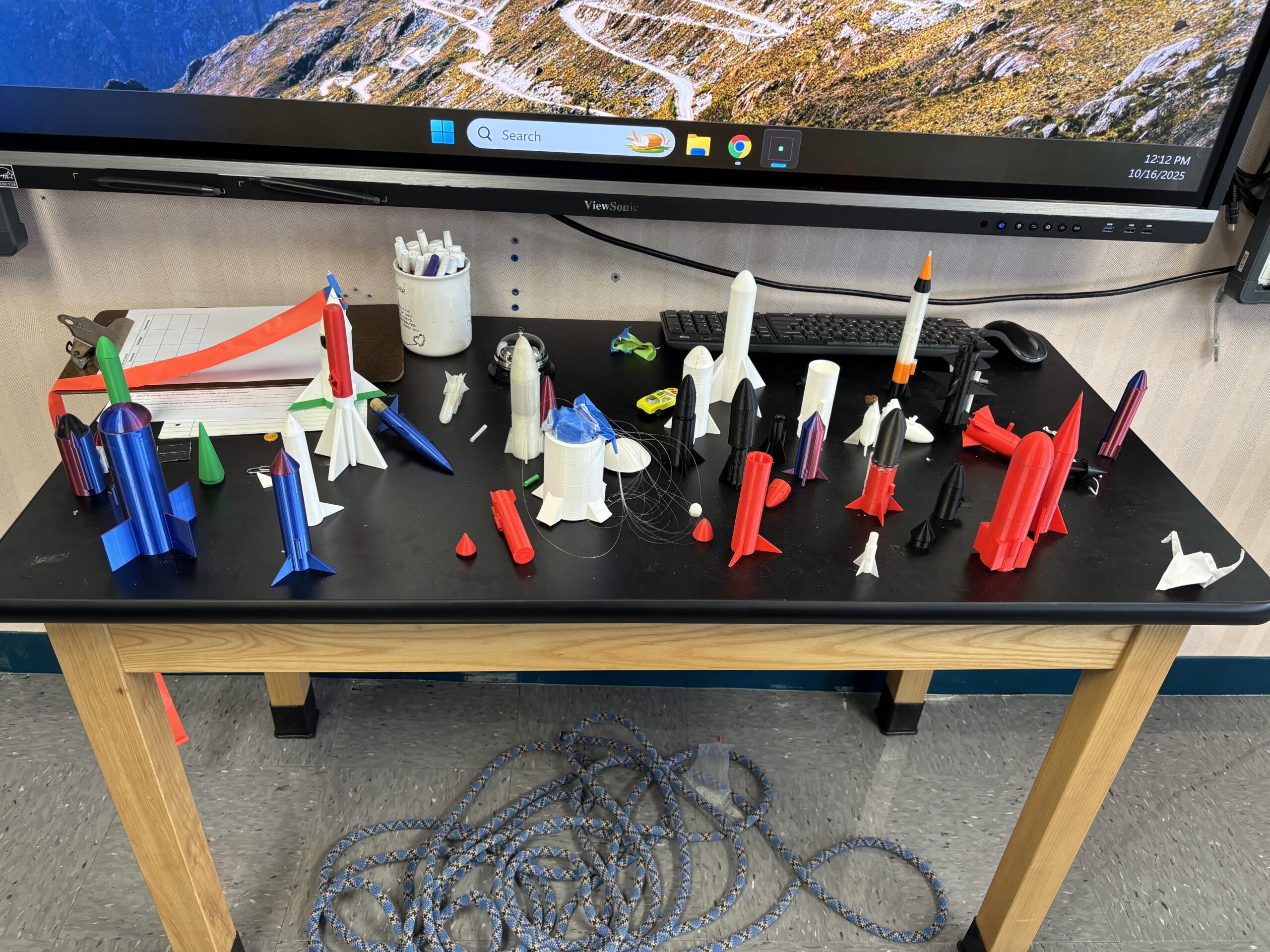 A wide range of 3D-printed rockets sit on top of a classroom table.