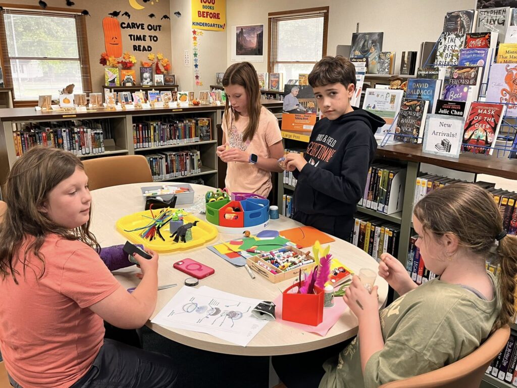 Students gather around a library table working on assembling their masquerade ball Sphero components.