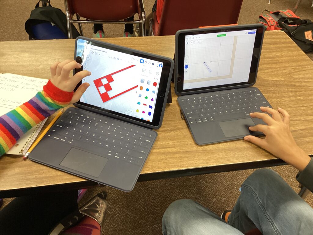 Two laptops show student designs. 
