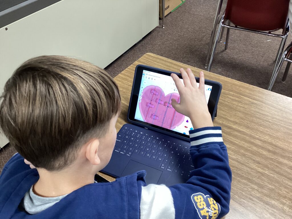 A student works on a heart design on a classroom tablet. 