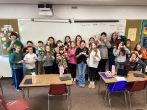 Students pose in front of the whiteboard with some of their 3D printed objects.