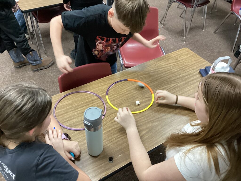 Students gather around a classroom table, playing with some of their prints. 