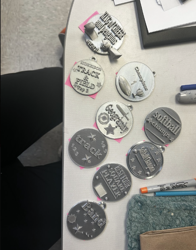 Some of the medals students printed. They are circular and say things like "track", "band", softball champs", etc. 