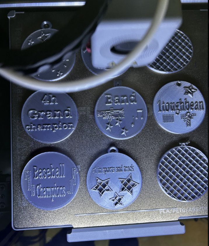 Some of the medals students printed. They are circular and say things like "band", "4th Grand Champion", and "baseball champion".