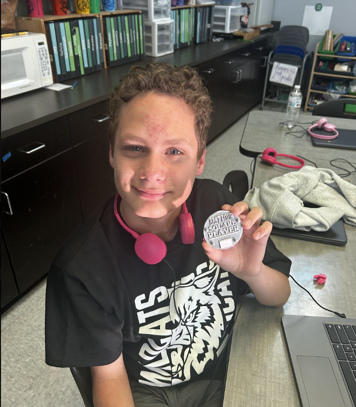 A student holds up their print, which is a circular medal that reads "Best Four Square Player."