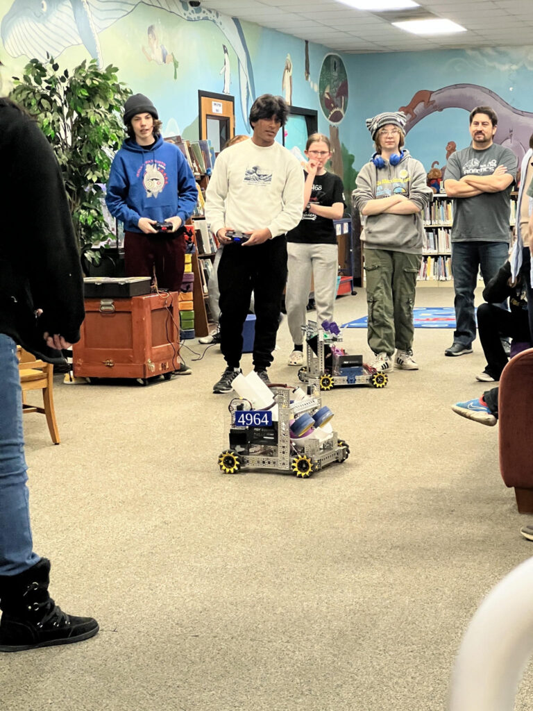 A photo from Rolla Public Library's robotics event, showing a group of people standing around a robot with one person controlling it. 