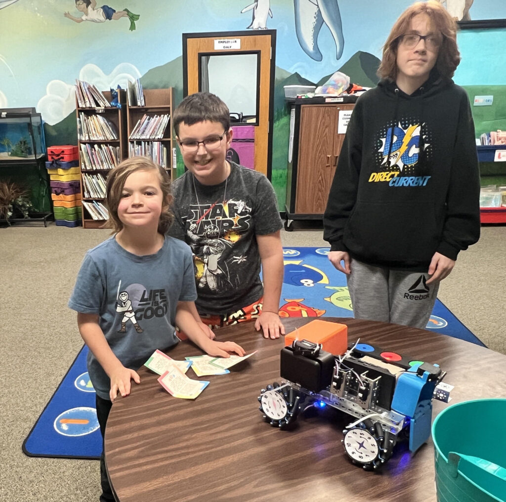A photo from Rolla Public Library's robotics event, showing three individuals at a table with a robot. 