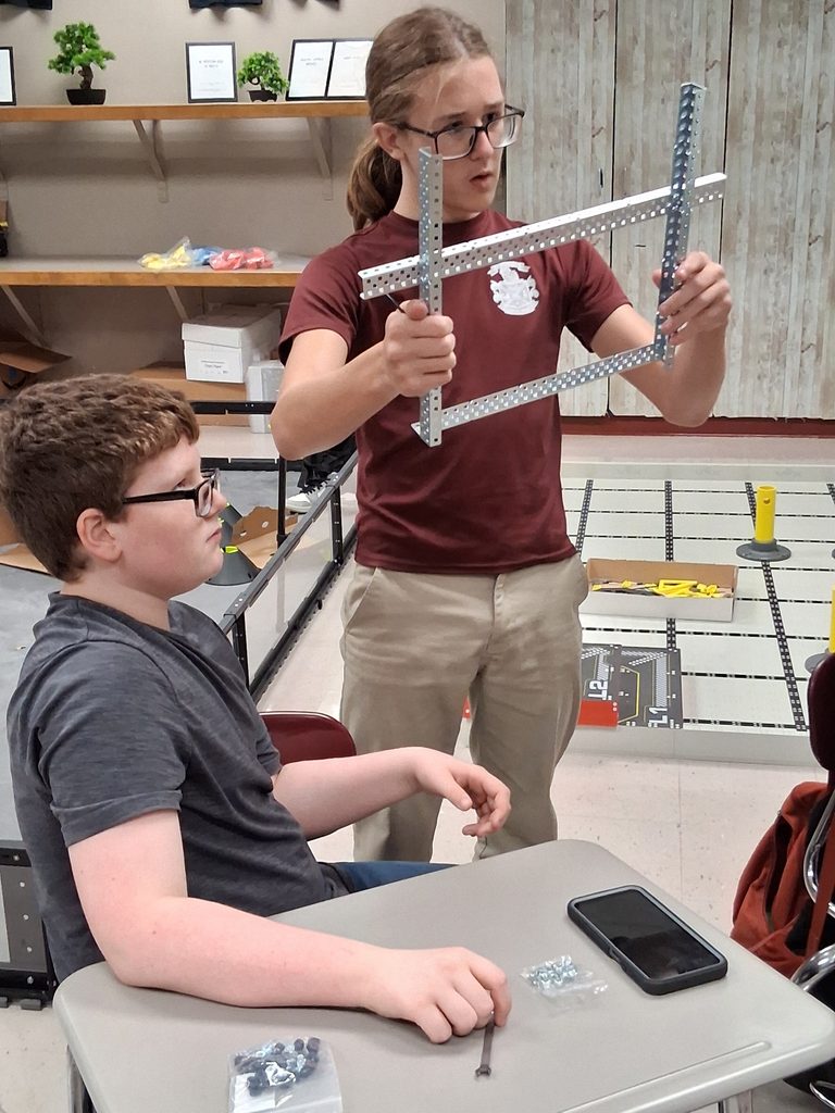 Two robotics team members work with VEX equipment, holding up pieces that they are constructing.